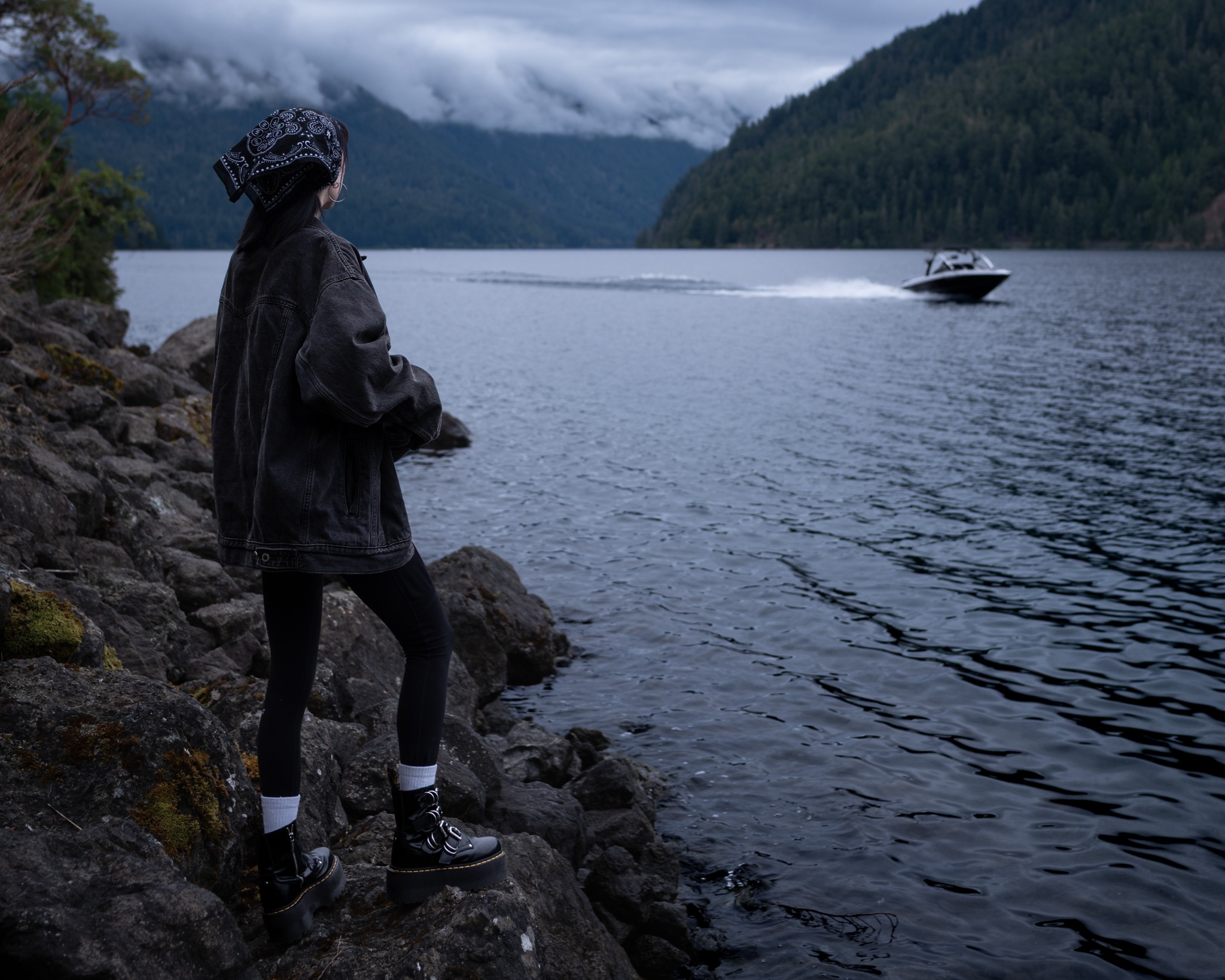A woman looks across a misty lake toward a passing motorboat.