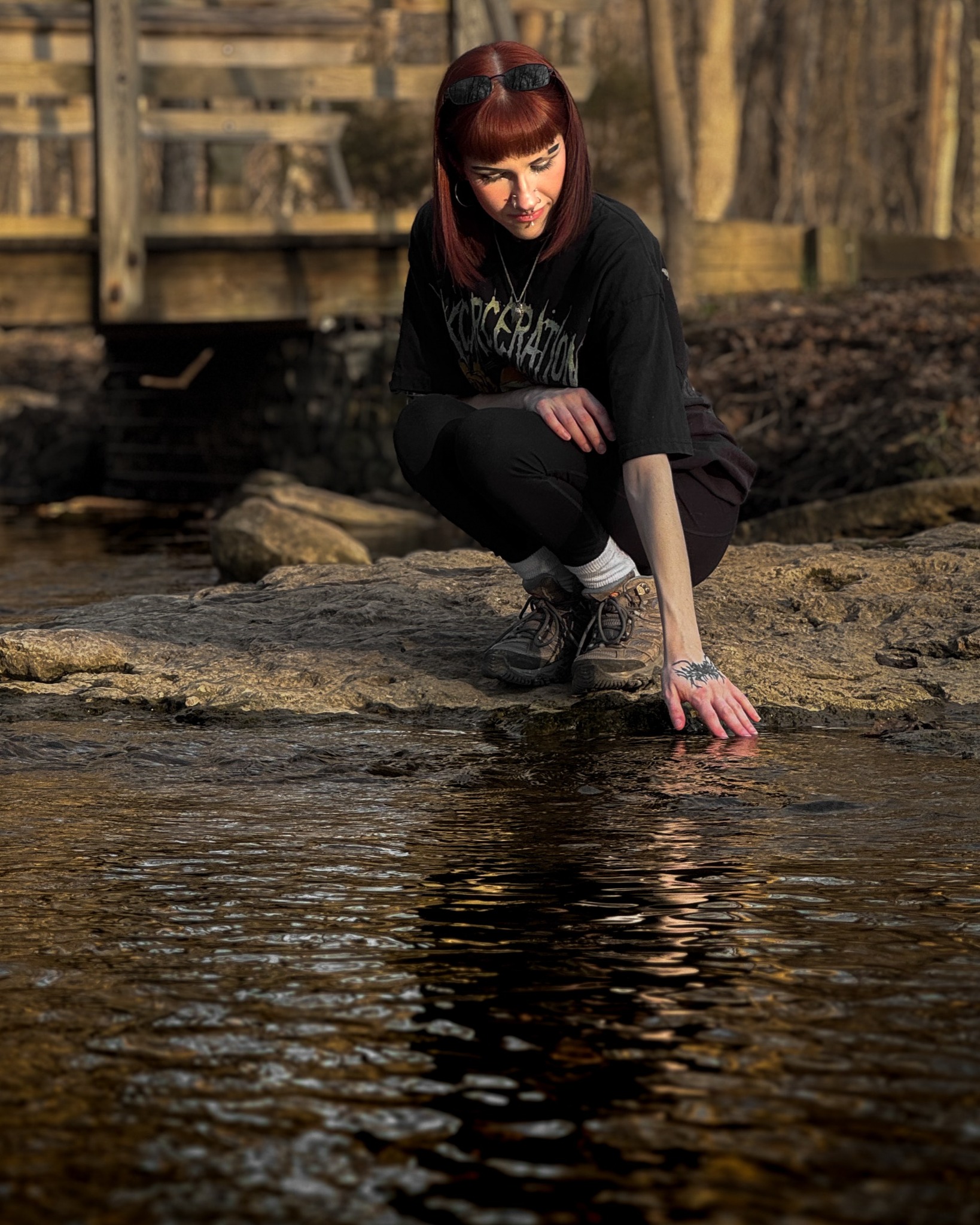 A woman reaches toward a shallow creek, her reflection extending through the water.